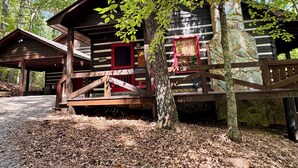 A rustic log cabin with a porch and a red door, surrounded by trees and a gravel path. - Beautiful Real Log Cabin.... Not your average cabin! Hot Tub. Wifi. Fire Pit (Blue Ridge)
