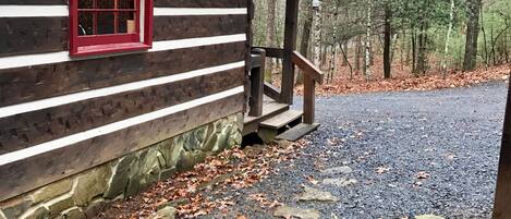 A log cabin with a red window and stone steps leading to a gravel path.