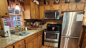 A kitchen with wooden cabinets, a stainless steel refrigerator, a microwave, an oven, and a granite countertop. - Beautiful Real Log Cabin.... Not your average cabin! Hot Tub. Wifi. Fire Pit (Blue Ridge)