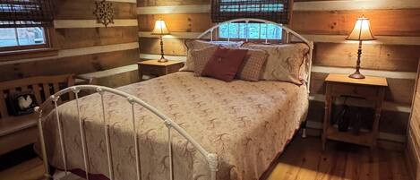 Une chambre confortable dans un chalet en rondins, avec un lit, deux tables de chevet, un ventilateur de plafond et une fenêtre donnant sur un paysage agréable.