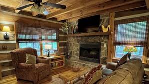 A cozy log cabin interior with a stone fireplace, wooden furniture, and a ceiling fan. - Beautiful Real Log Cabin.... Not your average cabin! Hot Tub. Wifi. Fire Pit (Blue Ridge)