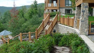 Un immeuble à plusieurs étages, doté d’une façade en pierre, de balcons en bois et d’un chemin en pierre menant à un espace extérieur couvert.