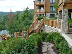 Un immeuble à plusieurs étages, doté d’une façade en pierre, de balcons en bois et d’un chemin en pierre menant à un espace extérieur couvert.