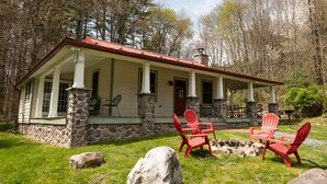Eine Holzhütte mit Steinelementen und rotem Dach, eine Veranda mit roten Adirondack-Stühlen und ein Steinkamin.