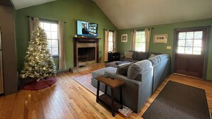 Ein Wohnzimmer mit Kamin, Weihnachtsbaum, Sofa und Fernseher.