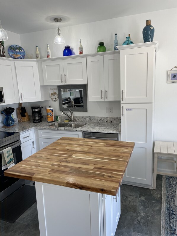 A modern kitchen with white cabinets, a wooden island, and various kitchen appliances.