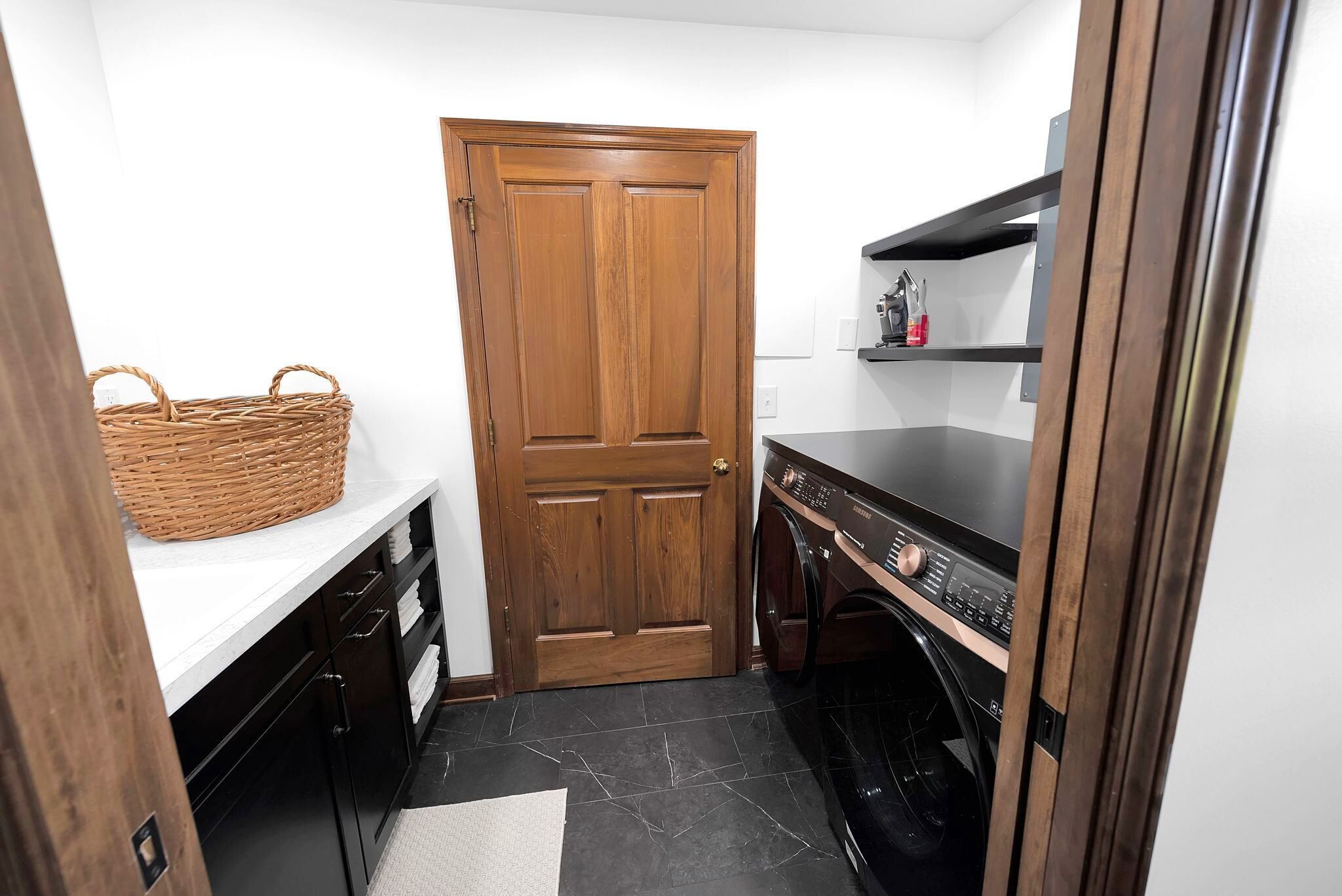 A compact kitchen with a wooden door, a washing machine, and a wicker basket on a countertop.