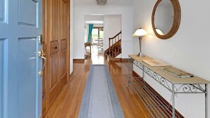 A hallway with wooden flooring, a blue door, a mirror, a lamp, and a small table with a book. - Superb British Colonial holiday home, greenhouse, outdoor deck, tropical garden (Barboursville)