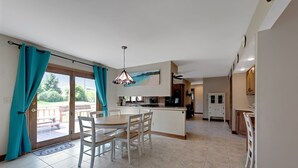 A modern kitchen with a central island, a dining area with white chairs, and a view of a deck through glass doors. - Superb British Colonial holiday home, greenhouse, outdoor deck, tropical garden (Barboursville)