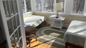 Une pièce confortable avec deux lits, un fauteuil en osier, une table avec une lampe et de grandes fenêtres donnant sur la forêt.