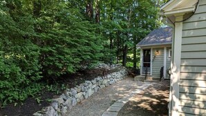 Un chemin de pierres mène à une maison dotée d’un porche, le tout étant entouré d’une végétation luxuriante.