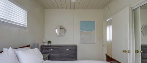 Une chambre à coucher comprenant un lit, une commode, un ventilateur de plafond, une fenêtre avec des stores et une porte.