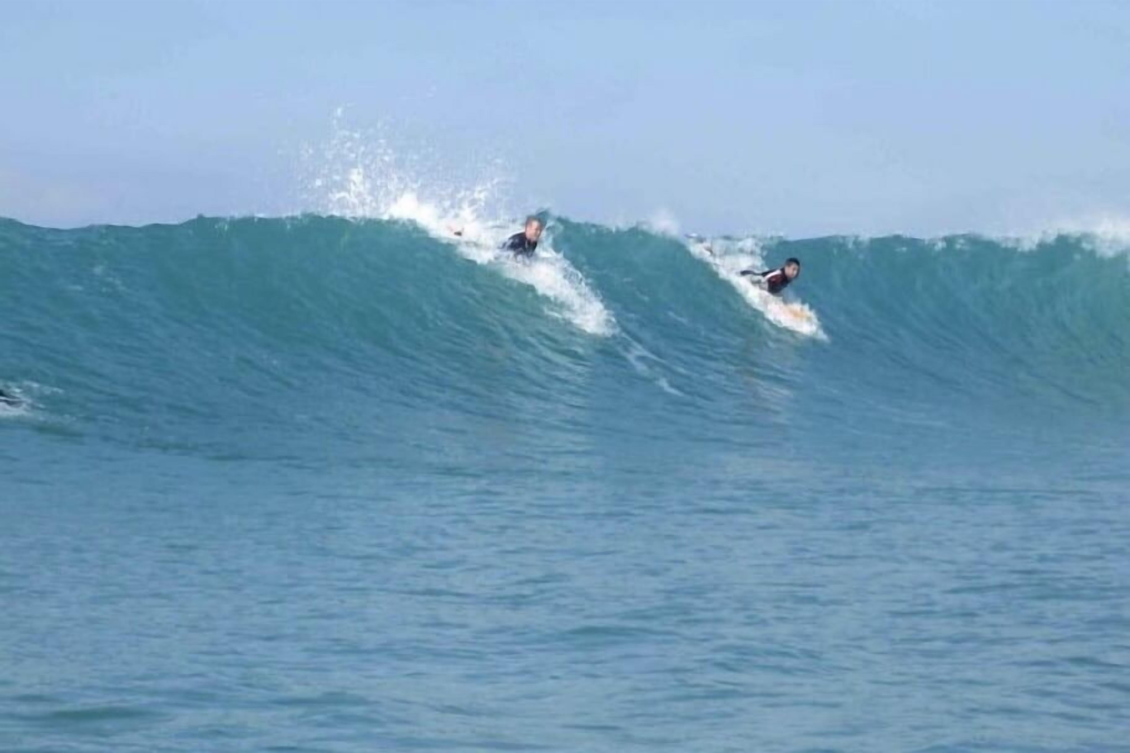 A large wave with two surfers riding it.