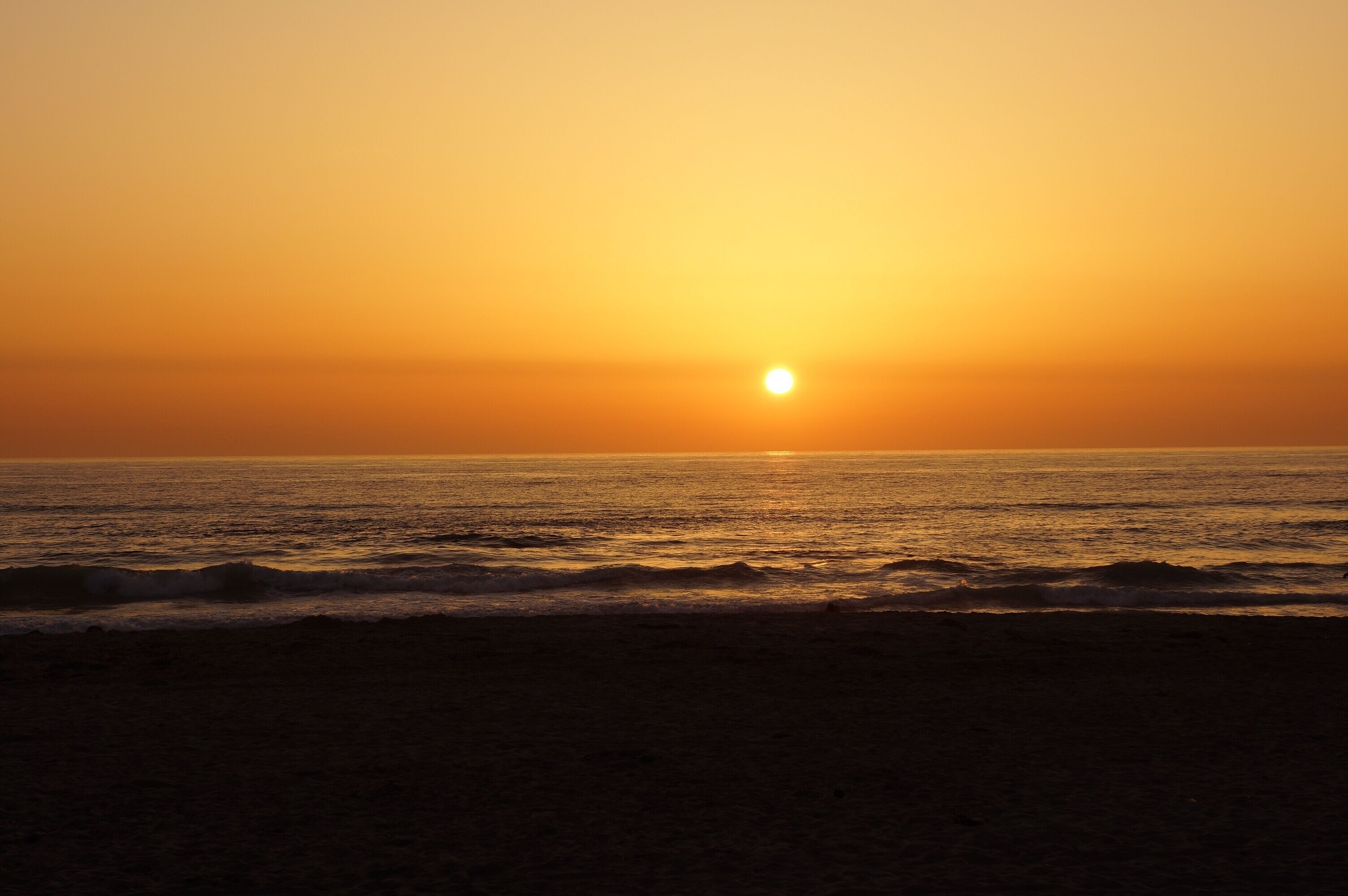 A sunset over the ocean with waves approaching the shore.