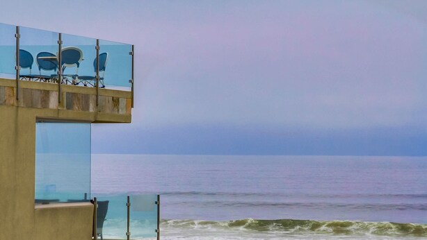 En bygning ved stranden med en glasbalkon med udsigt over havet.