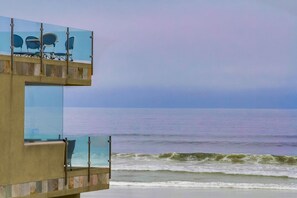 En byggnad som ligger vid stranden och har en balkong av glas med utsikt över havet.