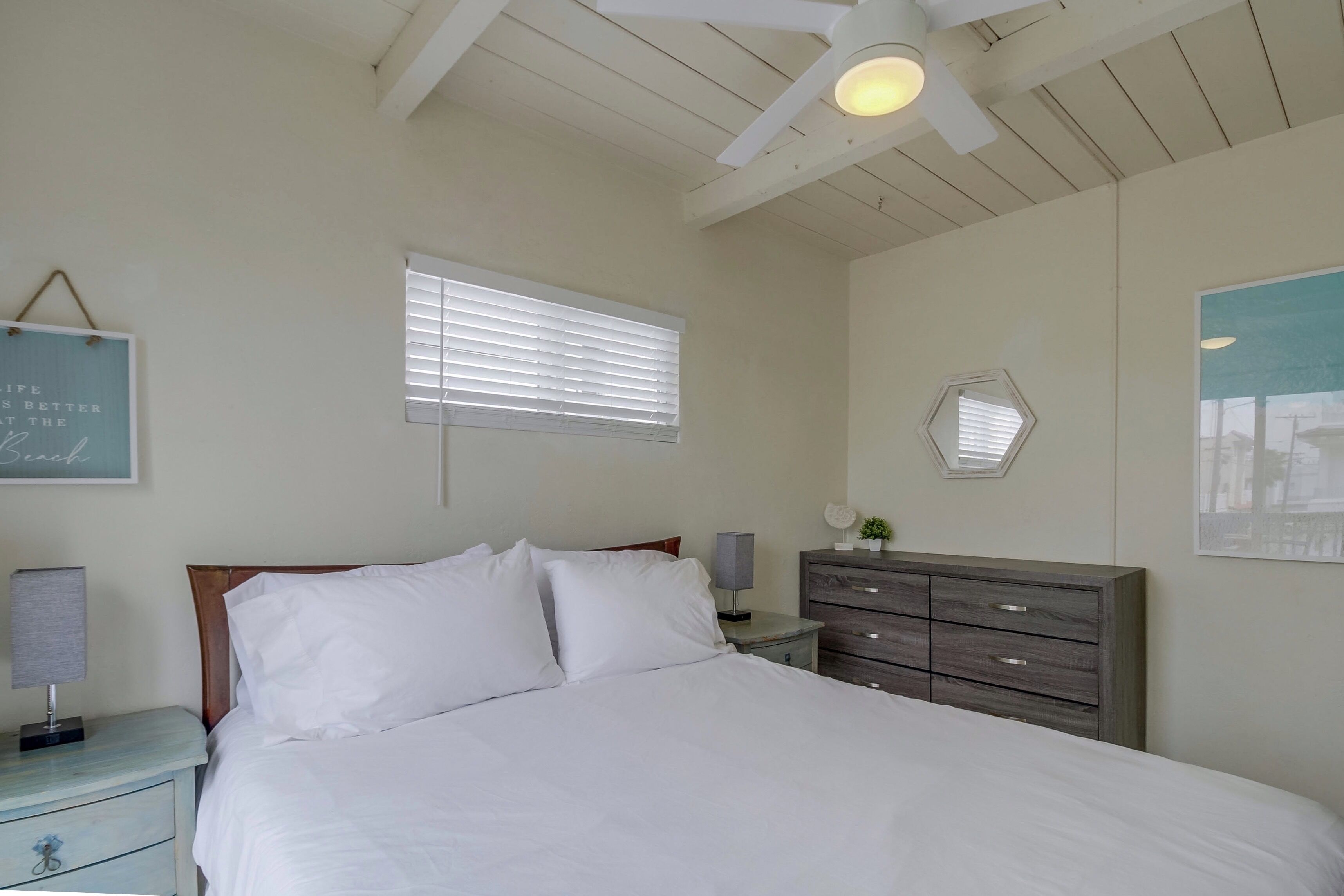 A bedroom with a bed, a nightstand, a dresser, a ceiling fan, and a window with blinds.