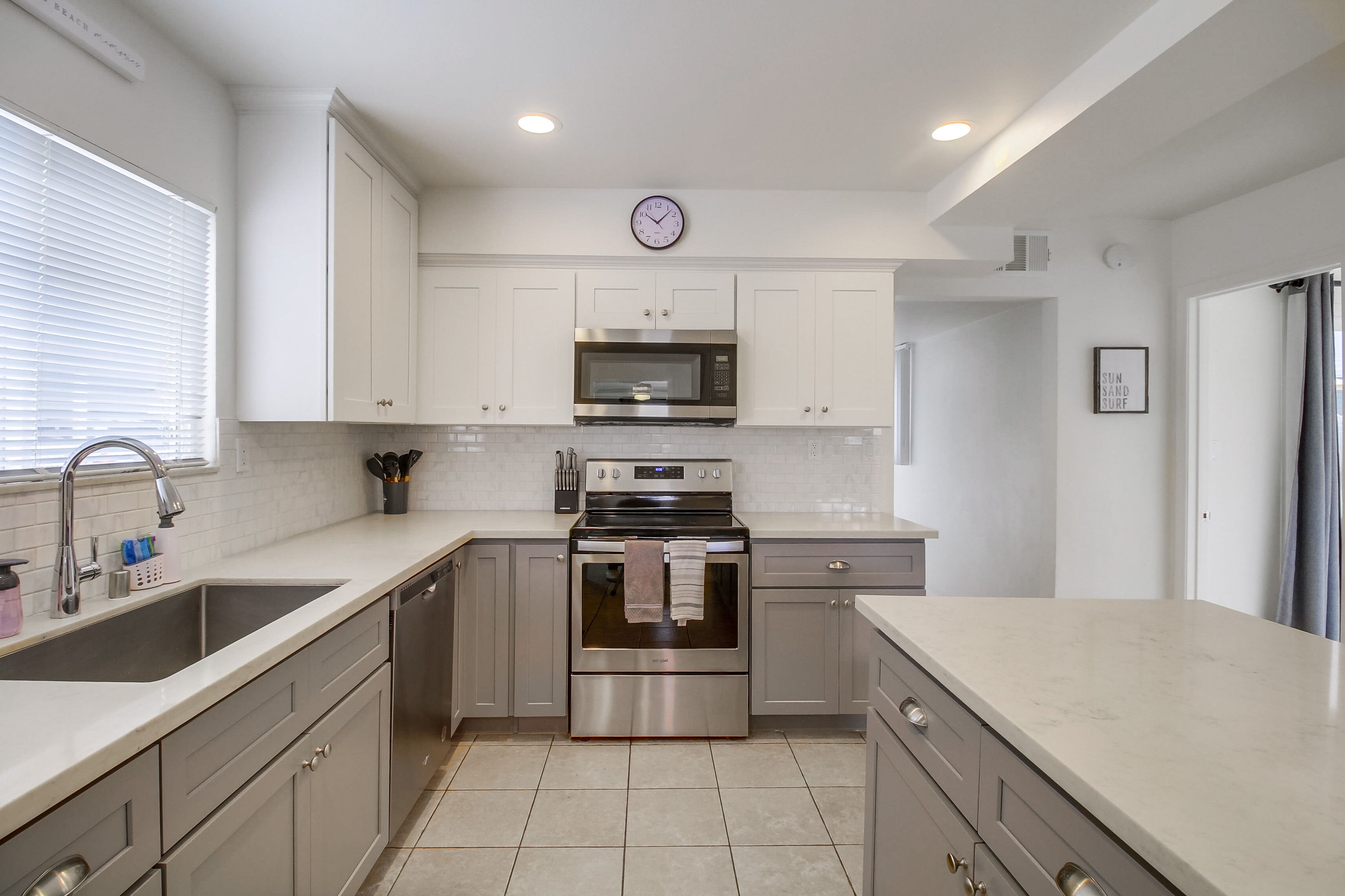 A modern kitchen with white cabinets, stainless steel appliances, and a large window.