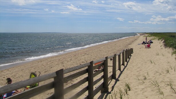 A beach with a wooden fence, sandy shore, and people relaxing. - Great SUMMER WEEKS Available! (New Seabury)