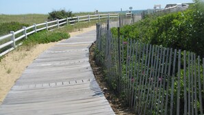 A wooden boardwalk leading to a beach with a white fence on one side and a metal fence on the other. - Great SUMMER WEEKS Available! (New Seabury)