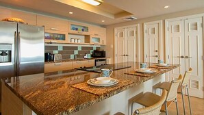 A modern kitchen with a granite countertop, stainless steel appliances, and a breakfast bar with chairs. - White Sand Beach Front, Turquois Blue Ocean View, Pools, Hot tub, Guarded,5 star (Christ Church)
