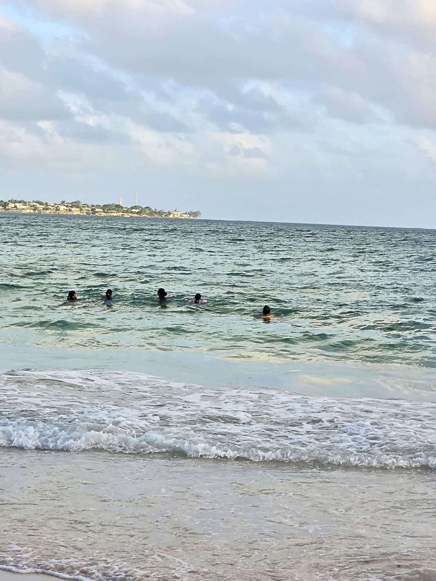 Une plage où des gens se baignent, et une côte lointaine avec des bâtiments.