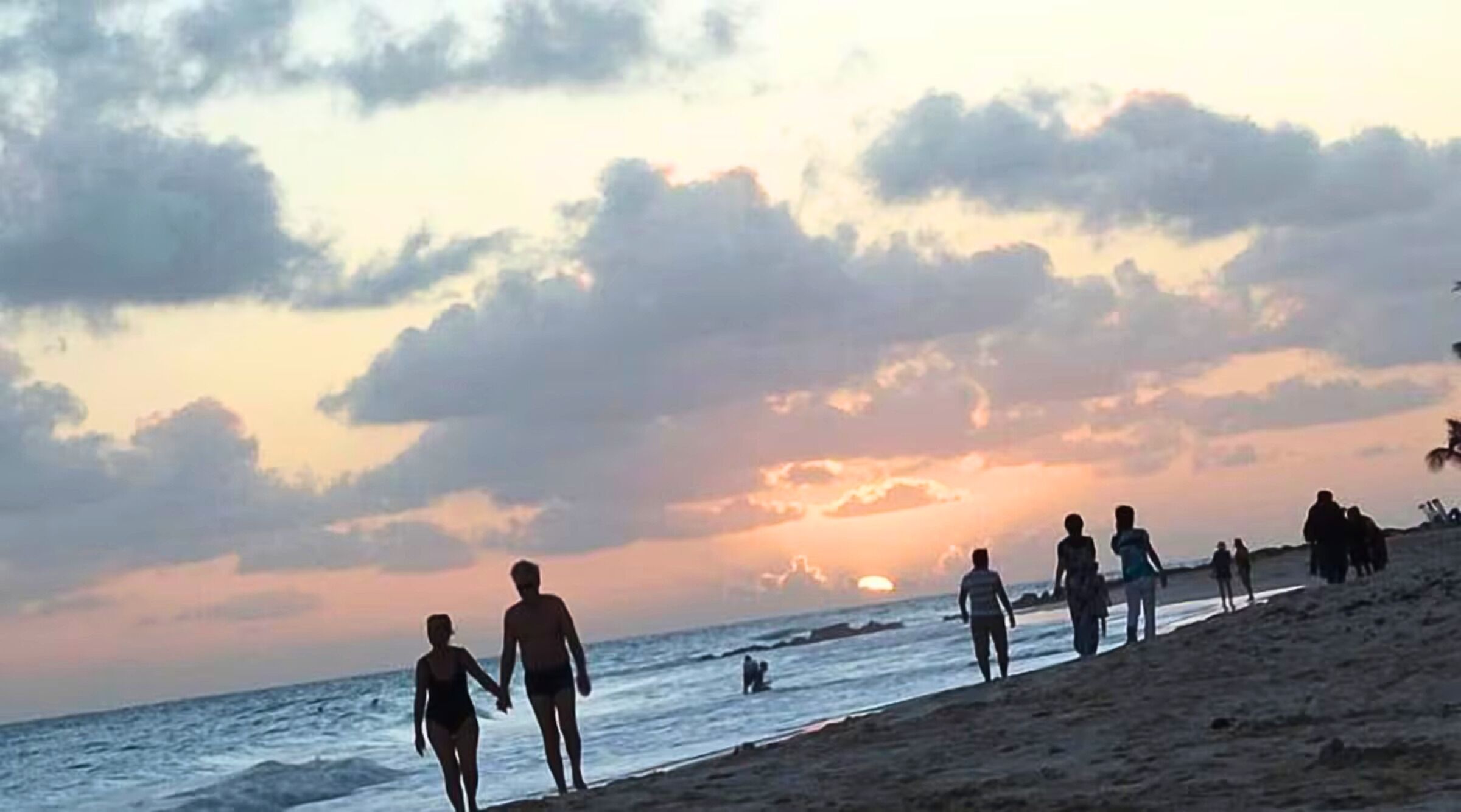 Uma praia com pessoas caminhando pela areia ao pôr do sol.