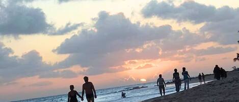 Uma praia com pessoas caminhando pela areia ao pôr do sol.