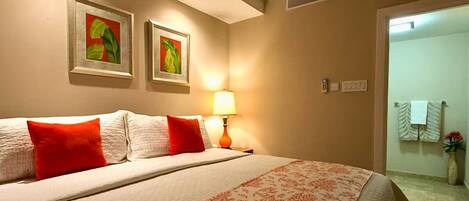 Een hotelkamer met een groot bed, twee rode kussens, een bedlampje en twee ingekaderde foto's aan de muur.
