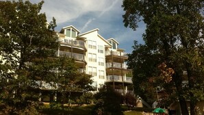 Un hotel de varios pisos con balcones, rodeado de árboles y una pequeña zona de parque.