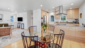 Una cocina moderna con armarios de madera, una isla central y una zona de comedor con mesa y sillas de vidrio.