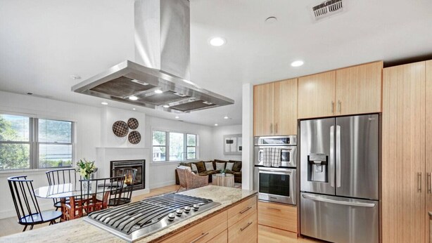Una cocina moderna con una isla central, electrodomésticos de acero inoxidable, armarios de madera y una chimenea.