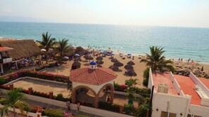 A beach with thatched umbrellas, palm trees, and a building with a tiled roof.