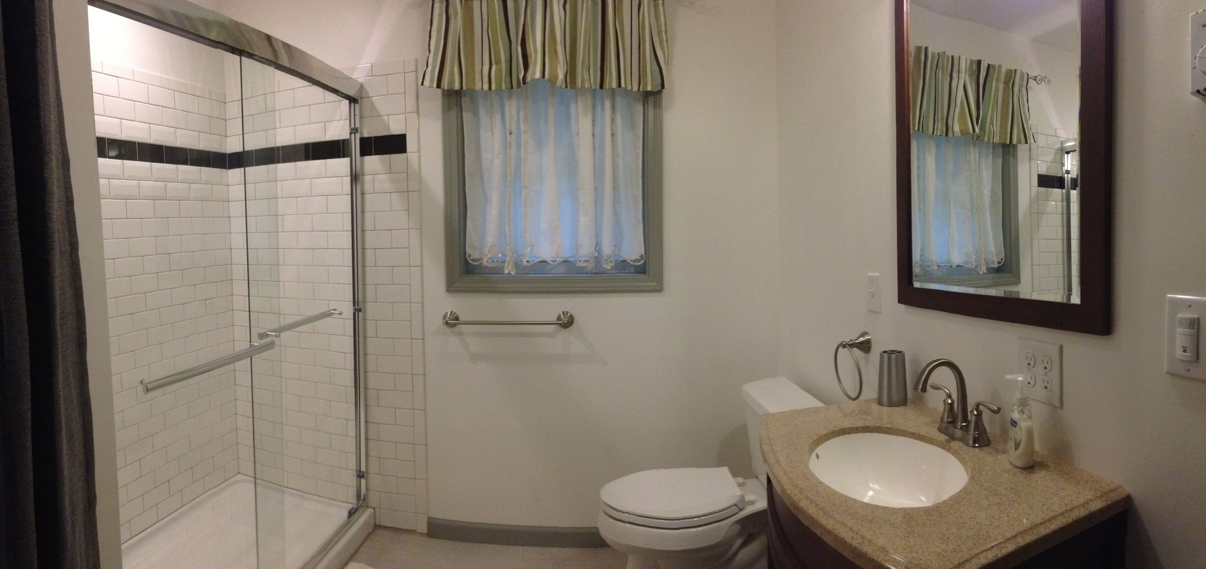 A bathroom with a glass shower enclosure, a toilet, a sink with a mirror, and a window with curtains.