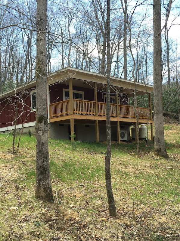 A cabin with a wooden deck and multiple windows, surrounded by trees.