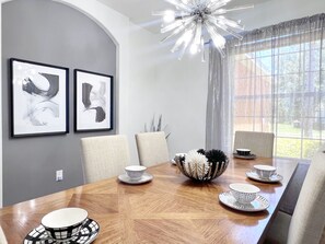 A dining area with a wooden table, chairs, and a chandelier. There are two framed artworks on the wall. - LAKEVIEW from Your Private Pool! - Relax & Create Memories - Resort Near Disney! (Davenport)