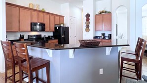A modern kitchen with wooden cabinets, a black refrigerator, and a central island with bar stools. - LAKEVIEW from Your Private Pool! - Relax & Create Memories - Resort Near Disney! (Davenport)