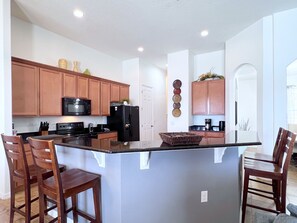 A modern kitchen with wooden cabinets, a black refrigerator, and a central island with bar stools. - LAKEVIEW from Your Private Pool! - Relax & Create Memories - Resort Near Disney! (Davenport)