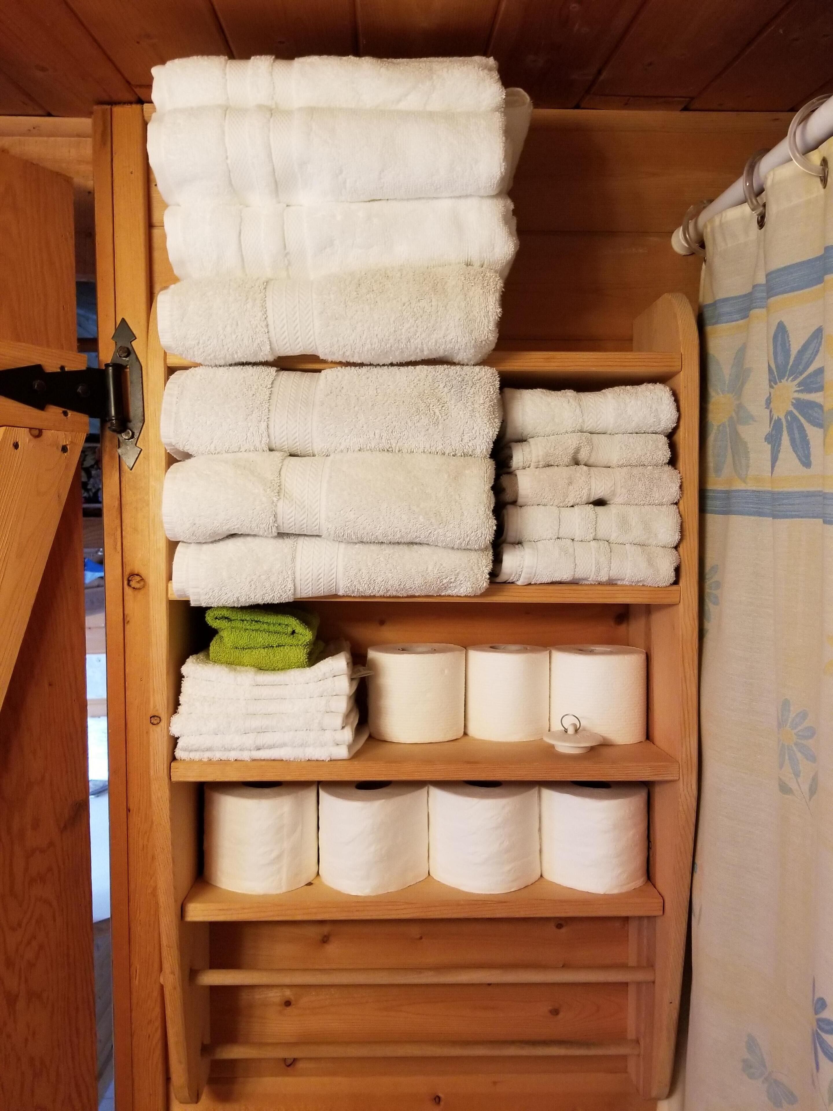 Un estante de madera con toallas blancas ordenadas y rollos de papel higiénico.