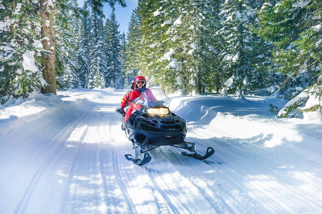 Ein Schneemobil auf einer verschneiten Straße, umgeben von Bäumen.