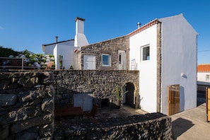 A stone house with a white exterior, a wooden bench, and a potted plant.