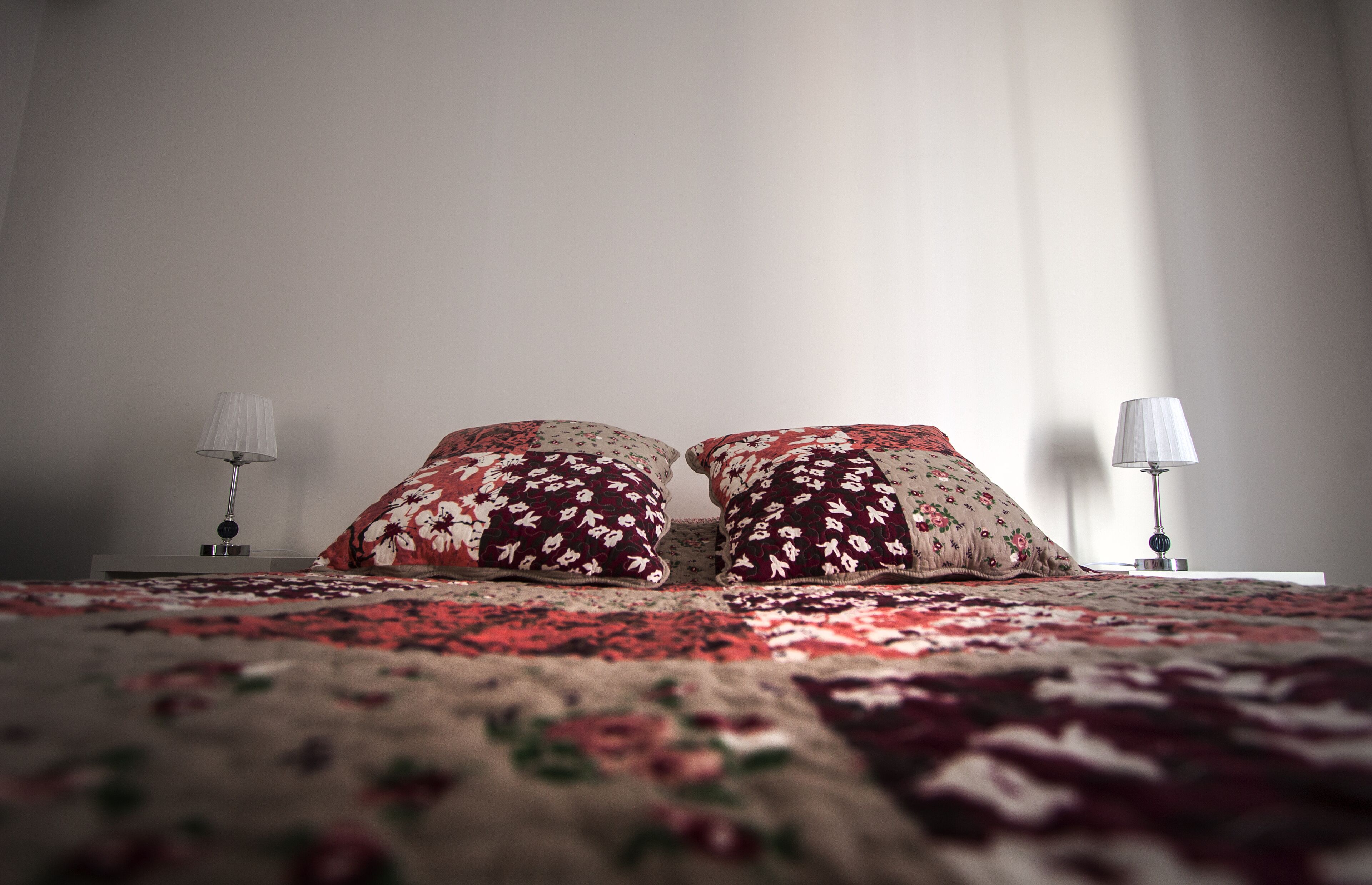 A bed with floral-patterned pillows and a matching bedspread, flanked by two bedside lamps on white nightstands.