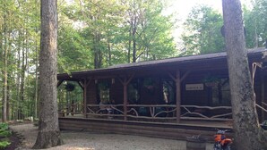 Une cabane en bois rustique, dotée d’un porche abrité et entourée d’arbres.