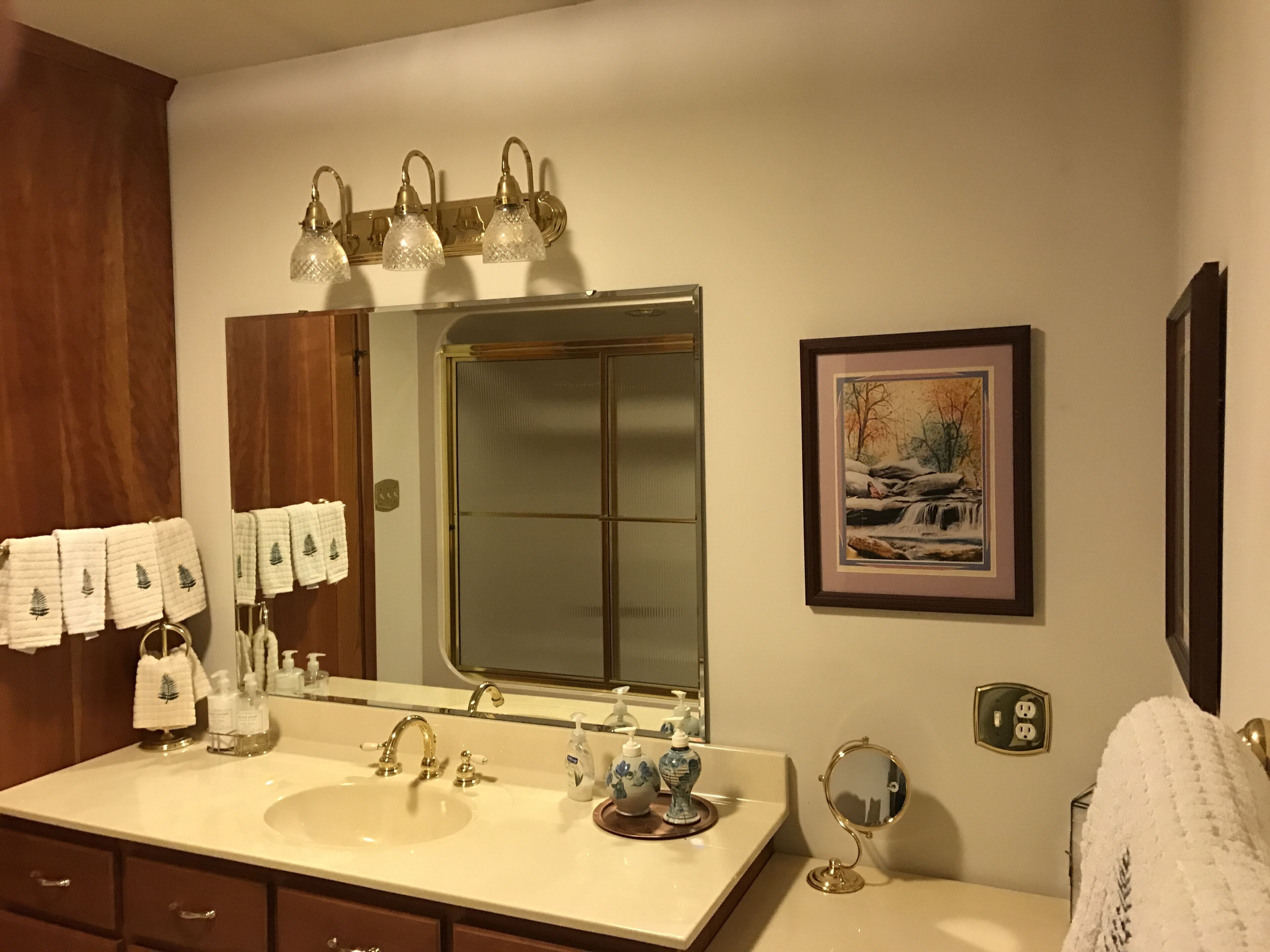 A bathroom with a double sink, a large mirror, a framed picture, and a towel rack with multiple towels.