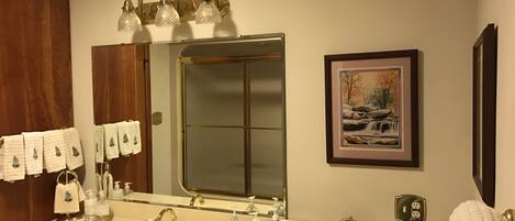 A bathroom with a double sink, a large mirror, a framed picture, and a towel rack with multiple towels.