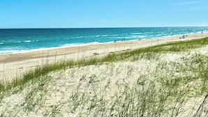 Ein Strand mit freiem Blick auf den Ozean, sandigen Dünen und grasbewachsenem Ufer.