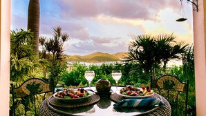 Une table dressée avec des assiettes remplies de nourriture et deux verres de vin blanc, donnant sur un paysage pittoresque avec des montagnes et une étendue d’eau.