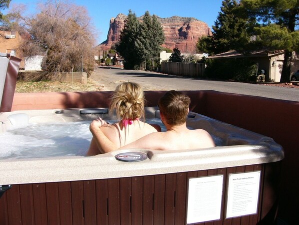 A hot tub with two people in it, surrounded by a wooden deck and a view of a mountain.