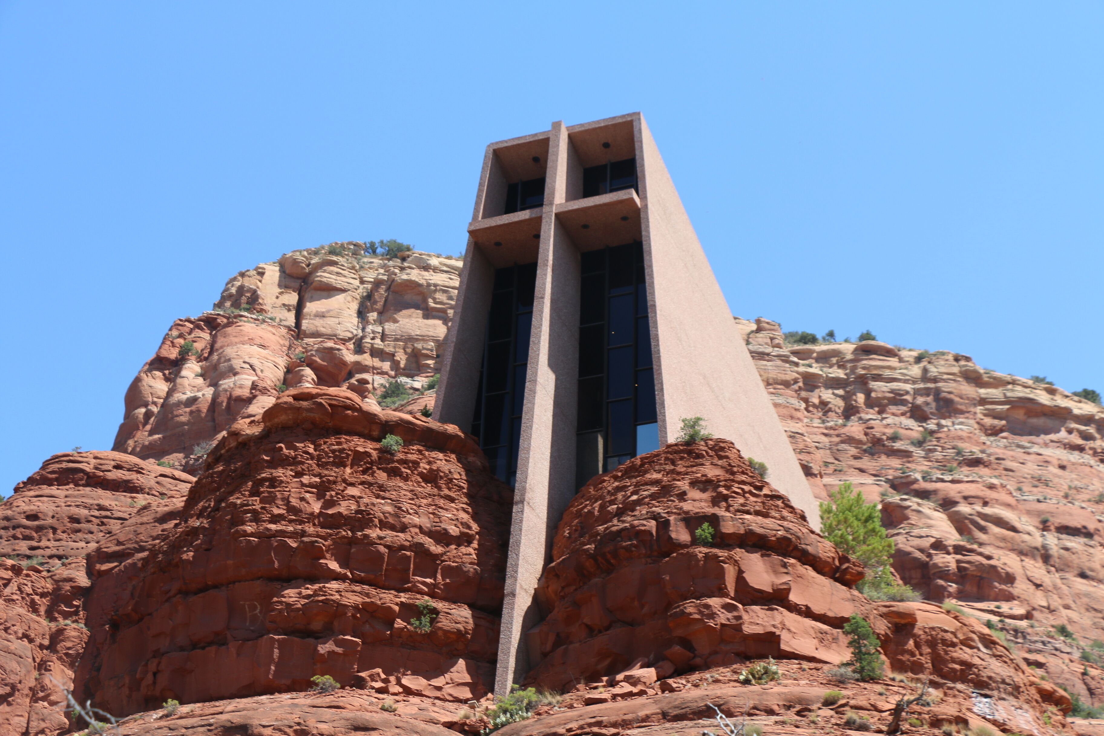 A building with a unique architectural design, featuring a tall, narrow structure with a flat roof and large windows, set against a backdrop of red rock formations.