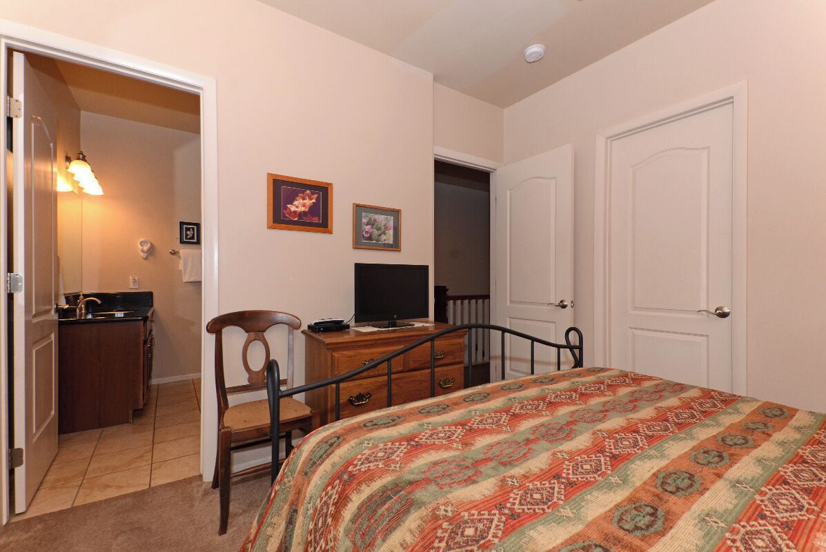 A bedroom with a bed, a desk with a computer, a chair, a dresser, and a door.